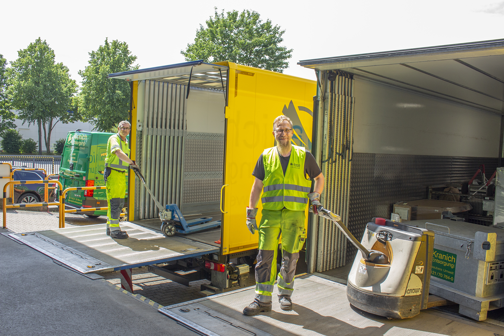 Zwei Männer mit elektrischen Gabelstaplern stehen auf der Ladefläche zweier nebeneinander geparkter LKW